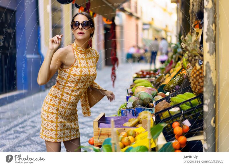 Stilvolle junge Frau steht vor einem Obstladen auf der Straße positiv trendy Mode Frucht Stadt Verkaufswagen Lächeln Brille Make-up nach vorne lehnen Inhalt