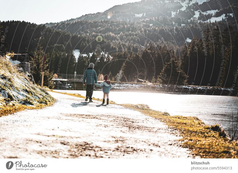 Zwei Kinder laufen zusammen an einem schönen November Nachmittag am Ufer eines Bergsees entlang Bruder Schwester Geschwister Laufen Wandern See Mädchen Junge