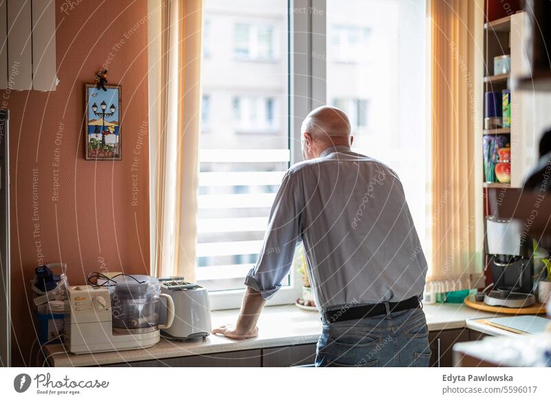 Ein älterer Mann steht an der Küchentheke in seinem Haus und schaut aus dem Fenster echte Menschen Senior älterer Erwachsener reif männlich Kaukasier heimwärts