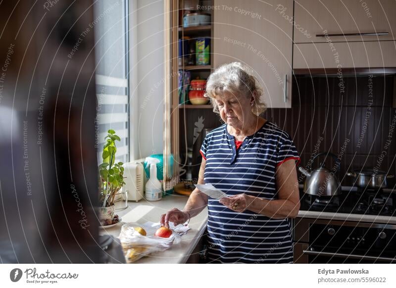 Ältere Frau, die nach dem Einkaufen zu Hause ihre Quittungen durchgeht Lebensmittel Geld zählen Rechnungen Lebenshaltungskosten Kosten beunruhigt Finanzplanung