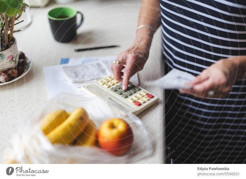 Ältere Frau, die nach dem Einkaufen zu Hause ihre Quittungen durchgeht Lebensmittel Geld zählen Rechnungen Lebenshaltungskosten Kosten beunruhigt Finanzplanung