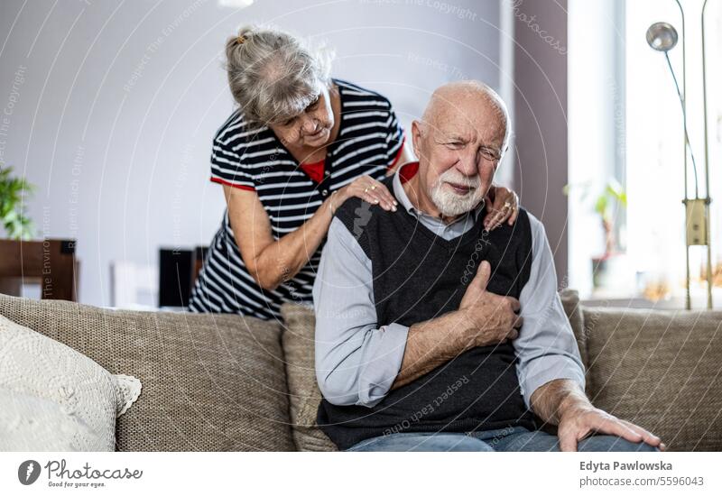 Älterer Mann leidet an Brustschmerzen, während seine Frau ihn tröstet echte Menschen Senior reif männlich Paar Zusammensein Kaukasier älter heimwärts Haus alt