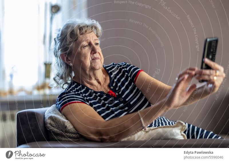 Ältere Frau sitzt auf der Couch und benutzt ein Mobiltelefon zu Hause echte Menschen Senior reif Kaukasier älter heimwärts alt Alterung häusliches Leben