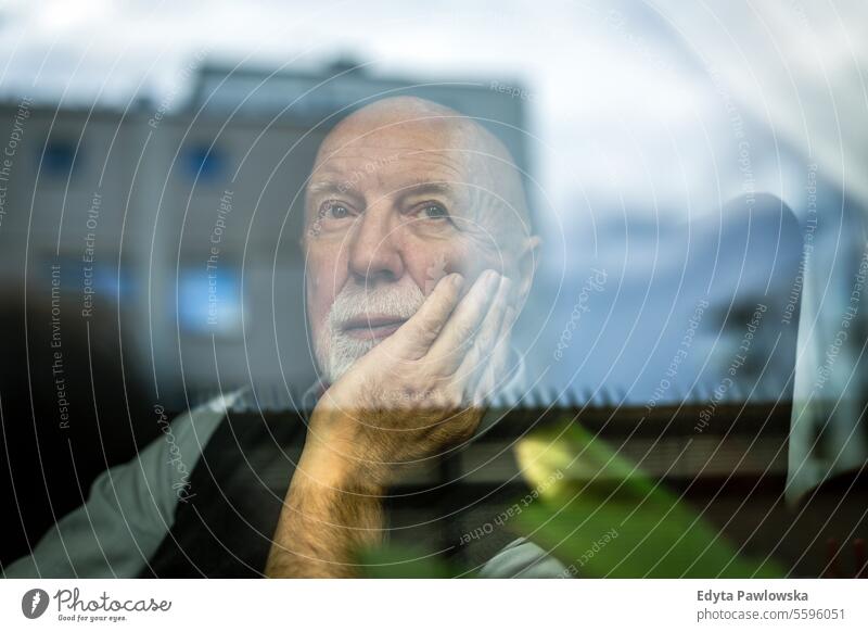 Porträt eines nachdenklichen älteren Mannes, der durch ein Fenster schaut echte Menschen Senior älterer Erwachsener reif männlich Kaukasier heimwärts Haus alt