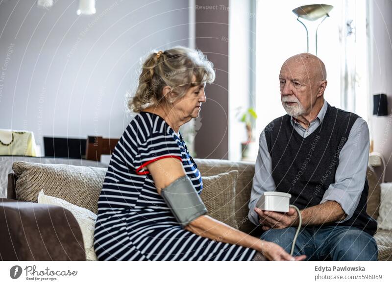 Älteres Ehepaar misst den Blutdruck, während es zu Hause auf dem Sofa im Wohnzimmer sitzt echte Menschen Frau Senior reif männlich Mann Paar Zusammensein