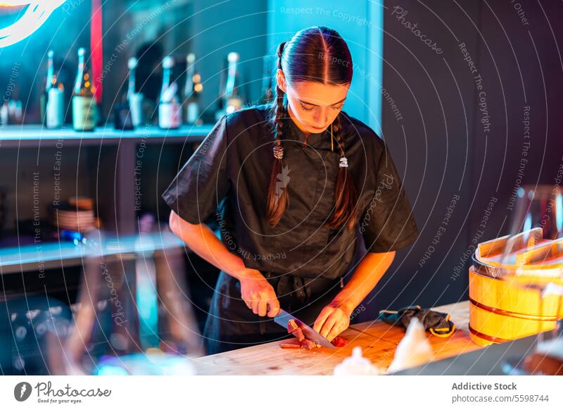 Selbstbewusste gelernte Köchin mit langen Zöpfen beim Schneiden und Zubereiten von Fleisch für das Abendessen an der Sushi-Bar Frau Küchenchef Messer
