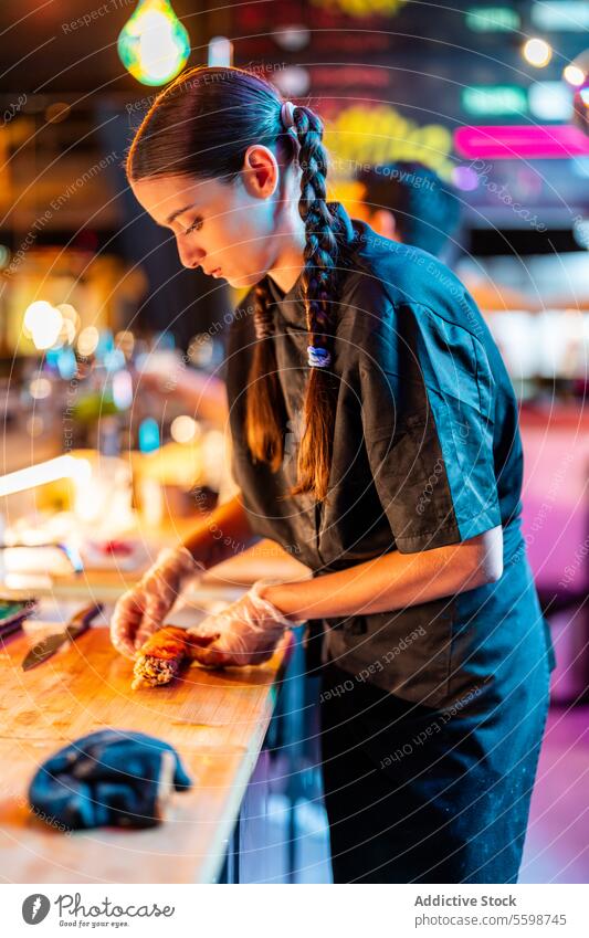 Seitenansicht eines selbstbewussten, erfahrenen Kochs in schwarzer Uniform und Handschuhen, der an der Theke steht und Meeresfrüchte im Bistro zubereitet Frau