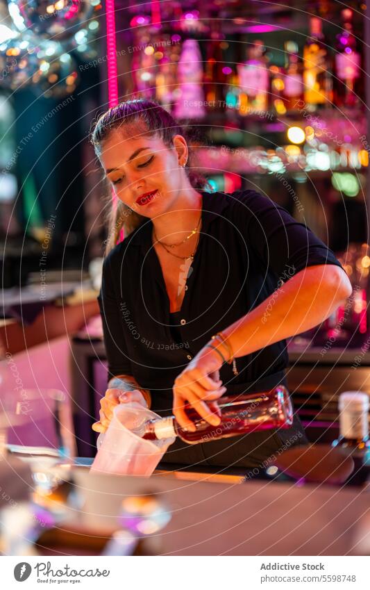 Lächelnde junge weibliche Barkeeperin steht und gießt ein Getränk in einen Becher aus einer Glasflasche in einer Kneipe Frau trinken Pub Flasche
