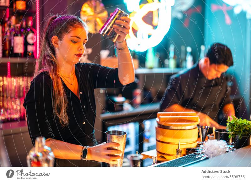 Seitenansicht eines selbstbewussten Barkeepers mit blondem Haar, der am Tresen steht und ein Getränk in einem Cocktailshaker in einer Bar zubereitet Frau