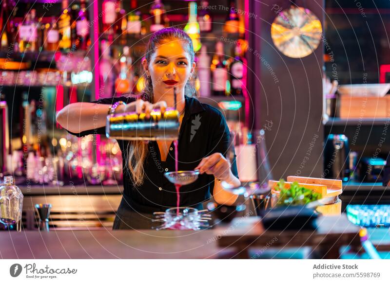 Schöne Bardame mit blondem Haar, die in die Kamera schaut, während sie einen Cocktail im Pub zubereitet Frau Barkeeper Gießen Schüttler Sieb selbstbewusst jung