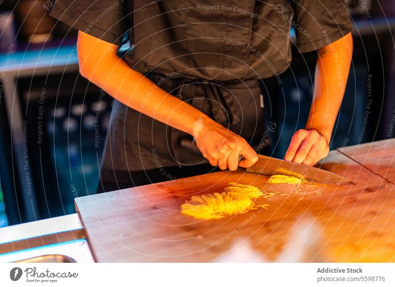 Geschulter anonymer Koch in schwarzer Uniform, der an der Theke steht, während er das Essen an der Sushi-Bar schneidet und zubereitet Frau Küchenchef Messer