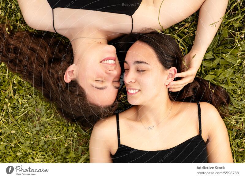 Glückliche Frauen, die in einem Moment der Zuneigung mit geschlossenen Augen im Gras liegen lachen lgbt Stolz lesbisch Paar Anschluss Liebe im Freien