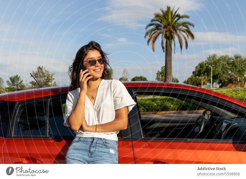 Glückliche Frau lehnt sich an ein Auto und spricht über ein Handy Anruf PKW Lehnen Smartphone attraktiv jung orange sprechend sonnig Sonnenbrille Mobile Lächeln