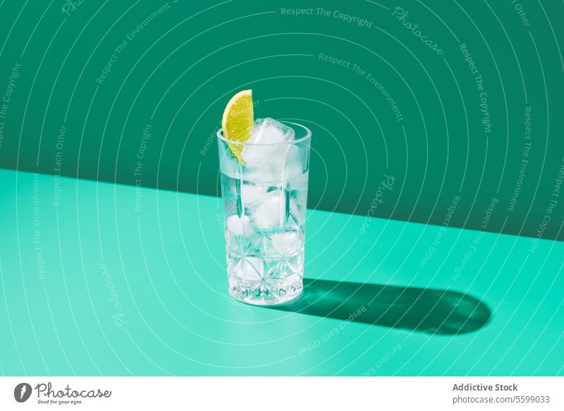 Erfrischendes Glas Gin Tonic mit Eis und Limette auf Grün Kalk Wasser Zitrone Schatten grün Hintergrund minimalistisch übersichtlich Erfrischung Getränk trinken