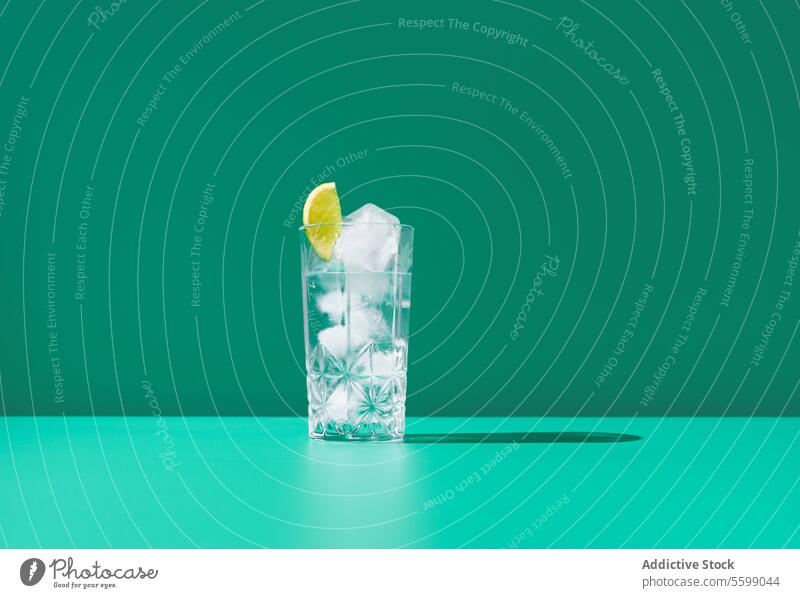 Erfrischender Gin Tonic in einem Glas mit Eis auf grünem Hintergrund Kalk Limonade Zitrone Scheibe kalt trinken Erfrischung Getränk Wasser übersichtlich Würfel