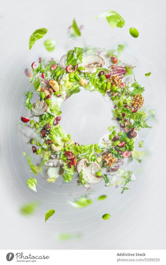 Kreisrahmen des fliegenden gesunden grünen Salats mit Salat, Nüssen, Bohnen, Dressing und Gemüse. Ausgewogenes veganes Essen mit Kopierraum. Levitation von Lebensmitteln