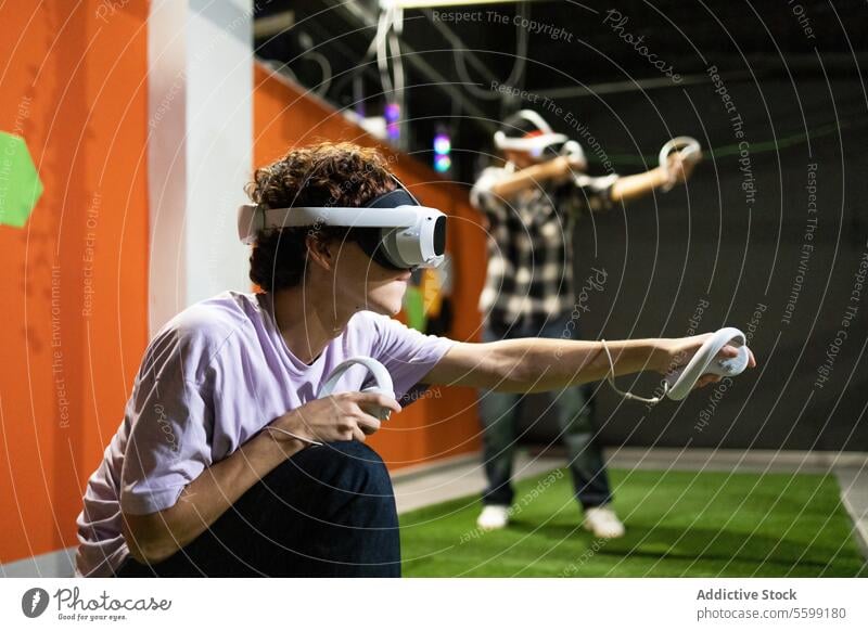 Junge Erwachsene tauchen in eine Virtual-Reality-Spielesitzung ein Virtuelle Realität VR Headset Regler Spielen Arkaden Technik & Technologie Erfahrung immersiv