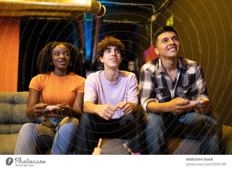 Drei junge, gemischtrassige Freunde sitzen auf einer Couch und spielen ein lustiges Videospiel. Männer Liege vielfältig Entertainment multiethnisch Regler