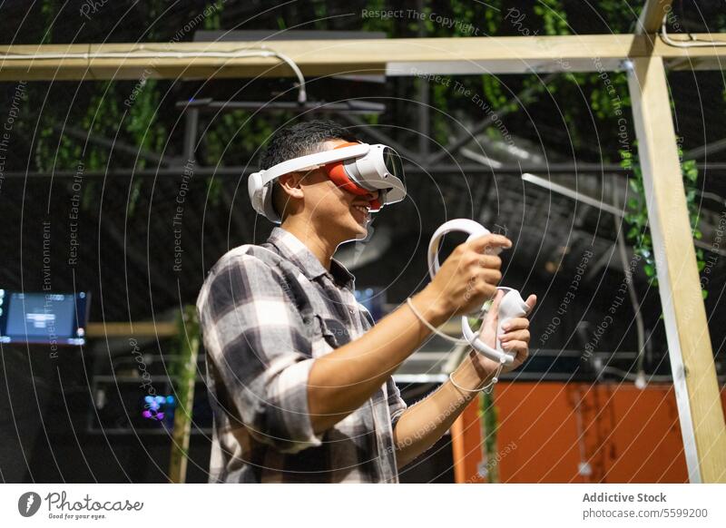 Seitenansicht eines jungen, aufgeregten Mannes, der mit einem VR-Headset und Controllern ein Virtual-Reality-Spiel spielt Virtuelle Realität