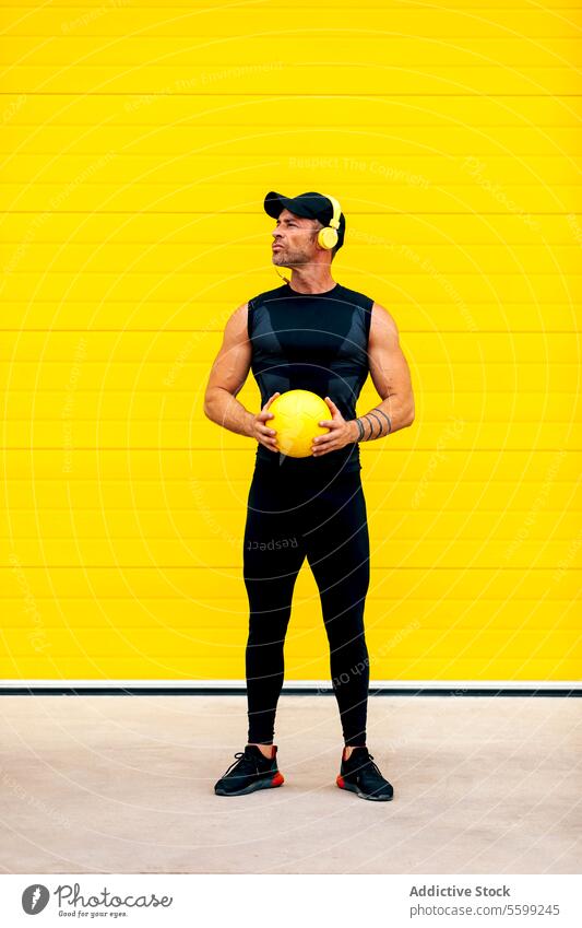 Selbstbewusster Sportler mit Ball in der Stadt stehend Athlet Kopfhörer Wegsehen selbstbewusst muskulös Beteiligung Straße Wand ernst spielen Spiel