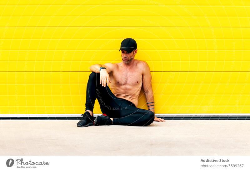 Müder Sportler ohne Hemd auf der Straße sitzend nackter Torso Sitzen erschöpft muskulös Denken Training aktiv müde Ganzkörper Athlet sich[Akk] entspannen gelb