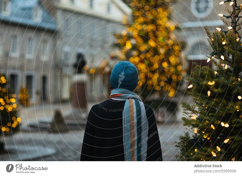 Nachdenkliche Figur bewundert die Weihnachtsbeleuchtung in einer Stadt in Quebec, Kanada Person Winter Hut Weihnachten Baum Feiertag urban Quadrat Rückansicht