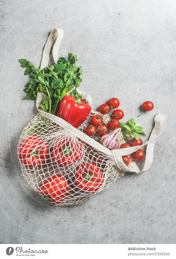Draufsicht auf verschiedene Gemüse und Kräuter in einer wiederverwendbaren plastikfreien Einkaufstasche auf einem grauen Betonküchentisch kunststofffrei Küche