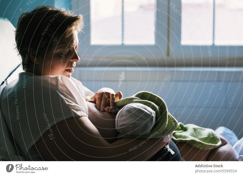 Frau, die ihr Baby stillt, sitzt auf dem Bett im Krankenhauszimmer. Mutter neugeboren Stillen Krankenpflege Raum stillen Mutterschaft mütterlich Brust Geburt