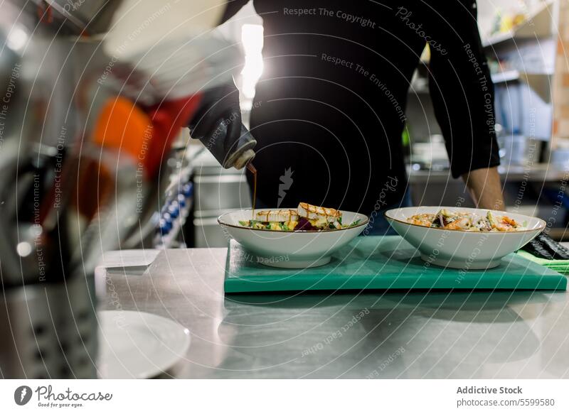Crop anonymer männlicher Koch in schwarzer Uniform serviert leckeren Salat mit gegrilltem Käse in der Küche eines Restaurants Mann Küchenchef Salatbeilage