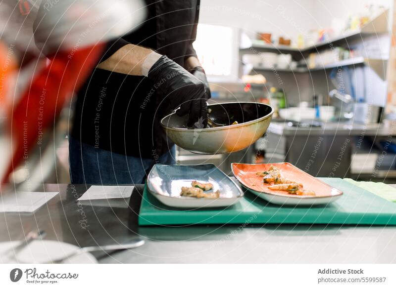 Seitenansicht eines anonymen männlichen Kochs mit Handschuhen, der am Tisch steht und köstliche gebratene Garnelen mit Gemüse auf Tellern in der Küche serviert