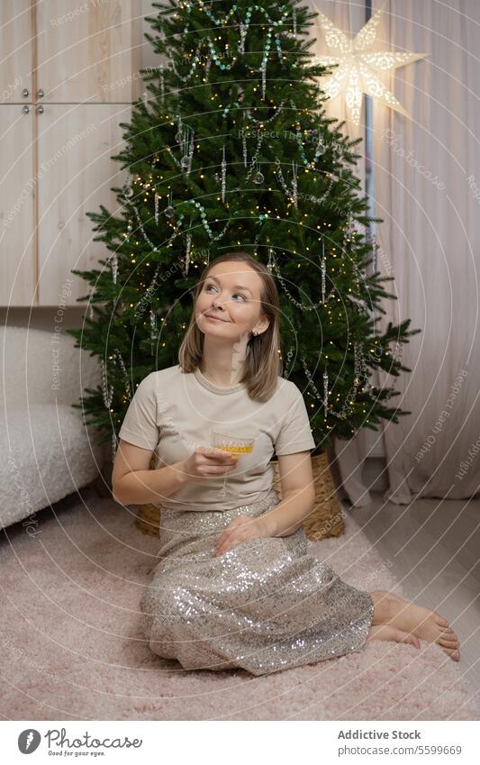 Fröhliches junges Mädchen sitzt an einem Weihnachtsbaum mit Sterndekoration und trinkt einen Cocktail Weihnachten Baum Dekoration & Verzierung festlich Saison