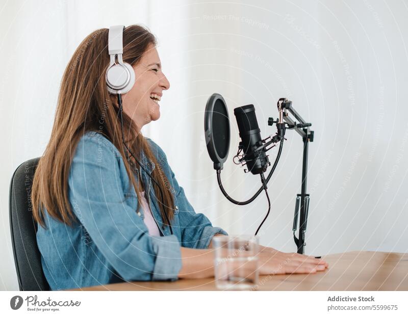 Fröhliche Frau mit Kopfhörern bei der Aufnahme eines Podcasts Aufzeichnen reden Lachen Spaß haben heiter Mikrofon Ausstrahlung Radio Atelier Wirt sprechen
