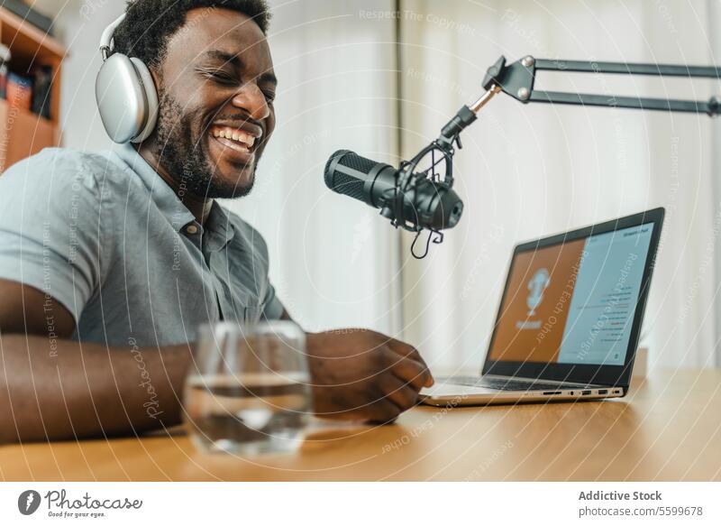 Schwarzer Mann mit Kopfhörern, der lachend einen Podcast aufnimmt Aufzeichnen Lachen Mikrofon Atelier aufgeregt Wirt Radio Spaß haben männlich ethnisch schwarz