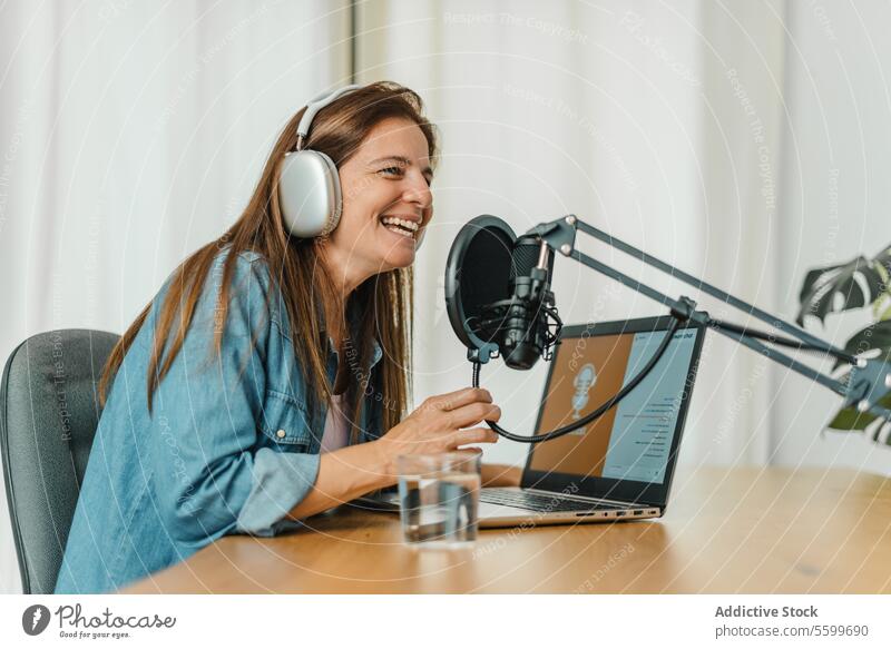 Glückliche Frau, die einen Podcast aufnimmt und in ein Mikrofon spricht reden Aufzeichnen Lächeln Radio Ausstrahlung Wirt Laptop Atelier sprechen unterhalten