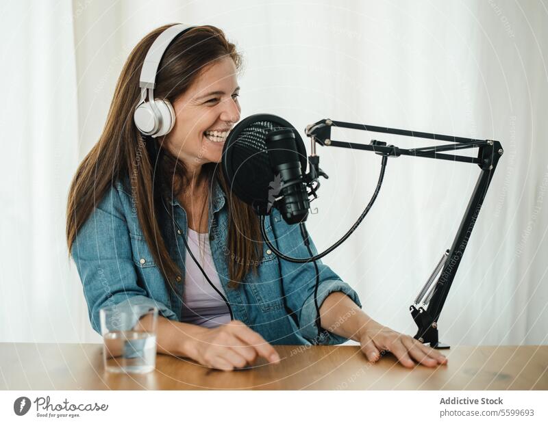 Glückliche Frau nimmt Podcast auf und lacht Aufzeichnen Mikrofon Lachen Spaß haben Radio Wirt live Ausstrahlung Atelier sprechen reden Lächeln Kopfhörer froh