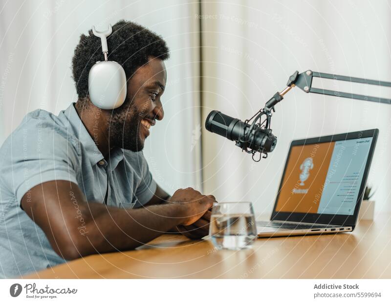 Lächelnder schwarzer Mann mit Laptop und Podcast-Aufnahme Atelier Ausstrahlung Aufzeichnen vorbereiten Mikrofon Kopfhörer männlich ethnisch Afroamerikaner Gerät