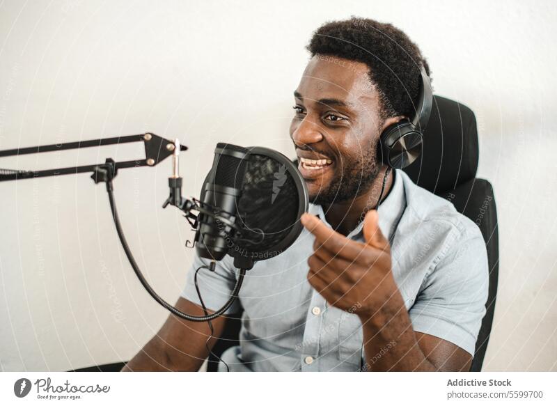 Begeisterter schwarzer Mann nimmt Podcast auf und spricht ins Mikrofon Aufzeichnen Radio Wirt reden Kopfhörer positiv Ausstrahlung männlich ethnisch