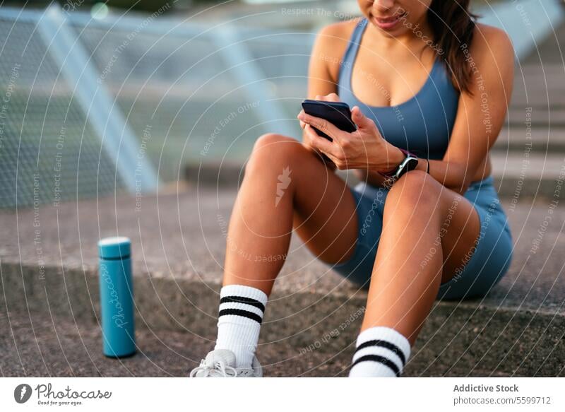 Konzept für einen aktiven Lebensstil mit einer lateinamerikanischen Frau am Telefon Lateinamerikaner Smartphone Training Pause Freitreppe Wasserflasche