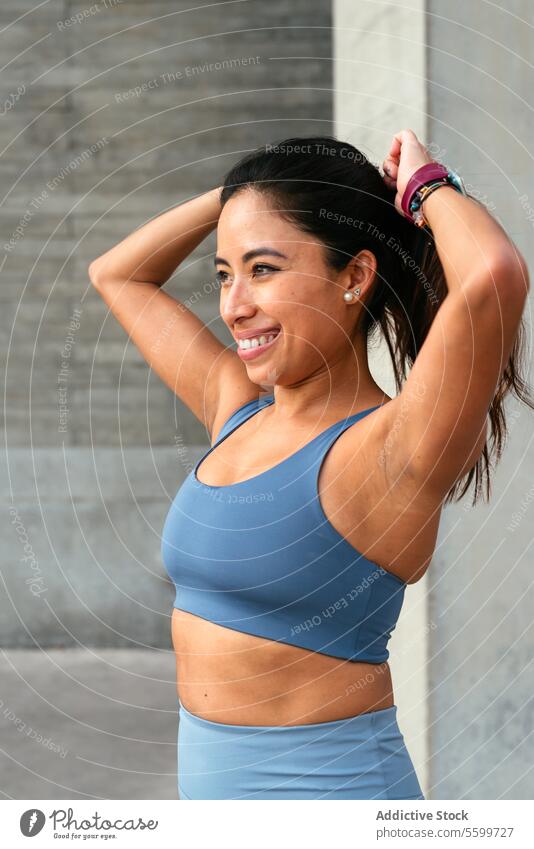Fröhliche lateinamerikanische Frau, die eine Fitnesspause genießt Lateinamerikaner Lächeln Training Pause Sportbekleidung Binden der Haare Glück aktiv Übung