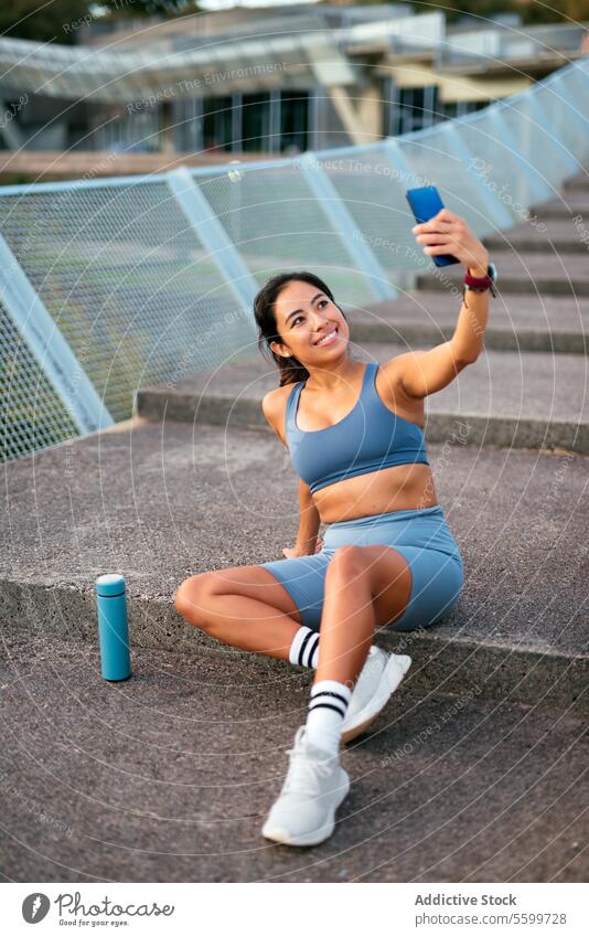 Lateinamerikanische Frau macht Selfie während Trainingspause Lateinamerikaner Sportbekleidung heiter Stadion Treppe Fitness Übung Wasserflasche sportlich