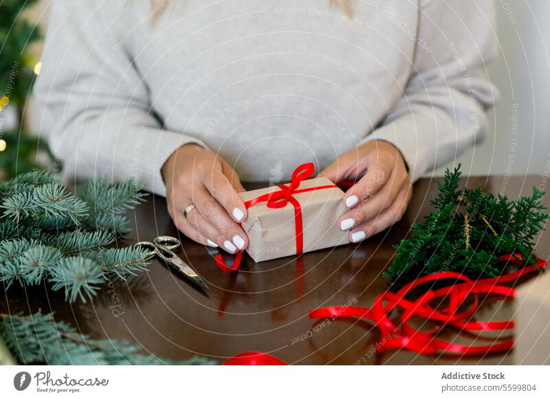 Eine unerkennbare Frau wickelt ein Weihnachtsgeschenk in Bastelpapier und einen Tannenzweig horizontal Bändchen Person Papier dekorierend im Innenbereich Glück