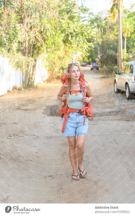 Junge reisende Frau, die mit einem Rucksack eine schmutzige Straße entlang läuft Aktivität Abenteuer sorgenfrei lässig selbstbewusst cool tagsüber Ausflugsziel