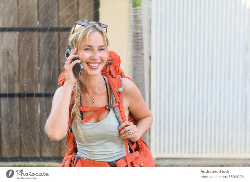 Fröhliche junge Frau mit Rucksack, die mit ihrem Smartphone spricht Abenteuer verschwommener Hintergrund heiter Kommunizieren Gespräch Textfreiraum Landschaft