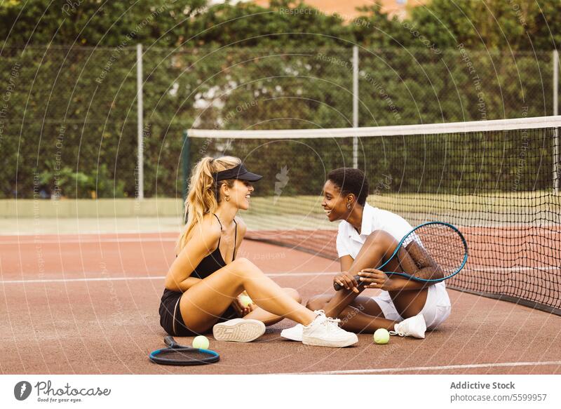 Zwei junge schöne Frauen unterhalten sich auf einem Tennisplatz neben dem Netz. Zwei Amateur-Tennisspieler machen eine Pause während eines Tennismatches. Athlet