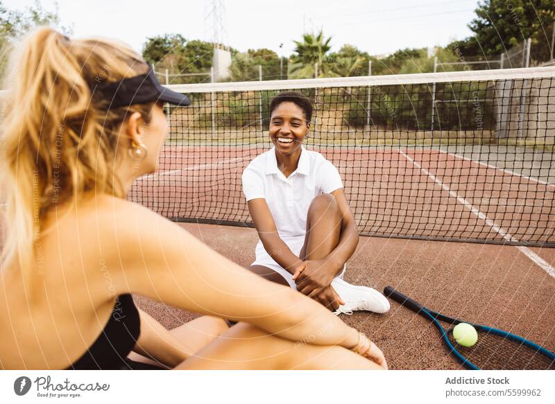 Zwei junge schöne Frauen unterhalten sich auf einem Tennisplatz neben dem Netz. Zwei Amateur-Tennisspieler machen eine Pause während eines Tennismatches. Athlet