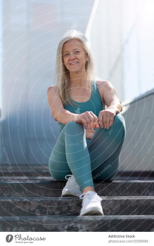 Aktive ältere Frau ruht sich nach dem Training auf den Stufen aus Senior aktiv Fitness Gesundheit Wellness Lächeln Sitzen Freitreppe graues Haar Sportbekleidung