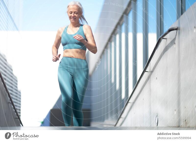 Ältere Frau joggt in städtischer Umgebung Senior reif Joggen urban Gesundheit Vitalität aktiv Lifestyle Übung Fitness sonnig im Freien rennen Athlet Wellness