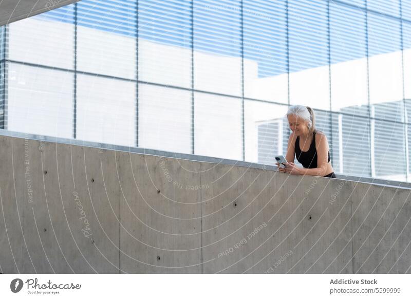 Reife Frau in Sportkleidung, die ein Smartphone in einer modernen Stadtumgebung benutzt reif Technik & Technologie Großstadt urban Konnektivität Lifestyle