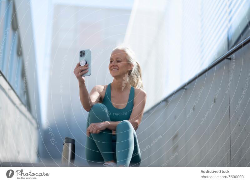 Lächelnde reife Frau nimmt Selfie nach dem Training Smartphone Fitness Sportkleidung ruhen im Freien Glück Flasche Wasser Übung Gesundheit Lifestyle Freizeit