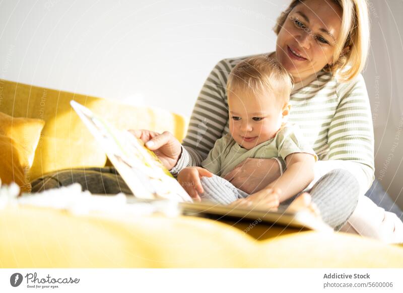 Mutter und Kleinkind genießen die Märchenstunde auf einer Couch lesen Buch Liege Bilderbuch achtsam gemütlich Lächeln sitzend gelb Familie Bonden Bildung Kind